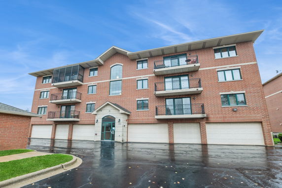 Front view of a multi-story brick apartment building with balconies and garage doors.