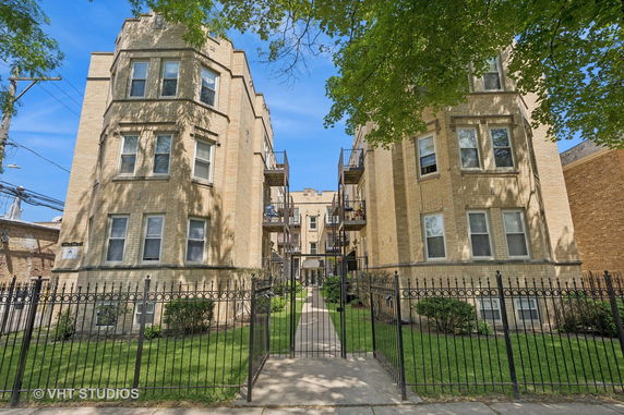 Front view of a multi-story apartment building with a gated entrance and balconies.