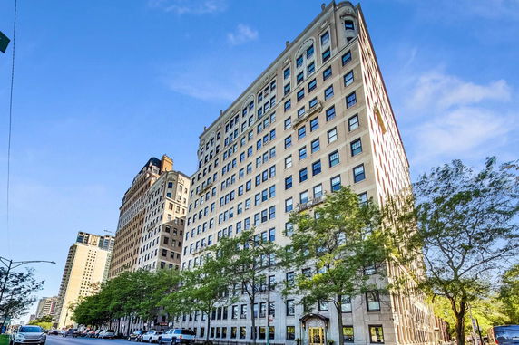 Front view of a multi-story residential building with numerous windows and trees along the street.