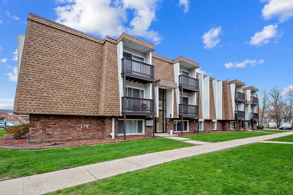 Front view of a multi-story apartment building with balconies and brown brick facade.