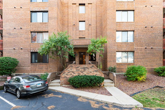 Front view of a brick apartment building with parking area and entrance steps.