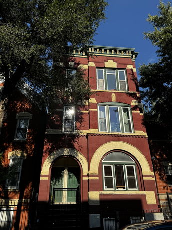 Front view of a multi-story brick building with arched windows and entrance.