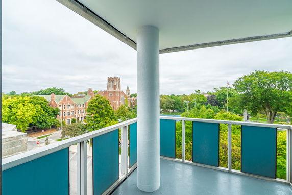 Panoramic view from a balcony showing a brick building and green trees.