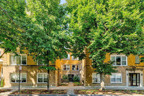 Front view of a multi-story brick building with large windows, surrounded by trees.