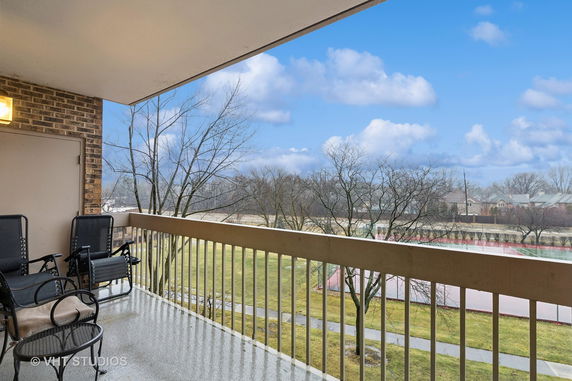 Balcony view with seating overlooking a tennis court and trees.