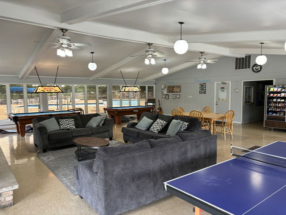 Interior view of a recreational club house with seating, pool tables, and table tennis.