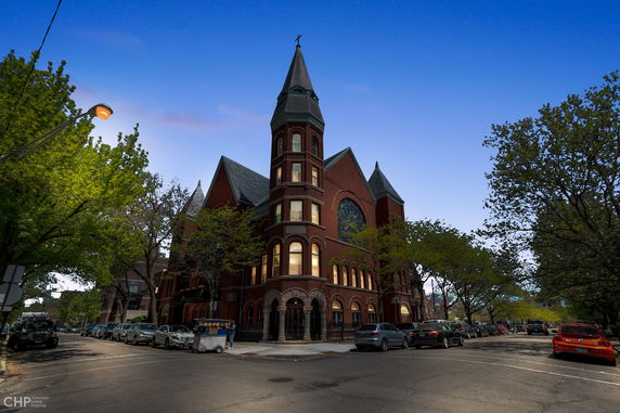 Front view of a large, multi-story brick building with a prominent tower and arched windows.