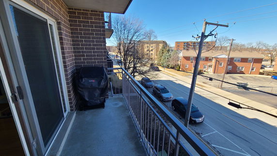 Balcony overlooking a residential street with parked cars and brick buildings.