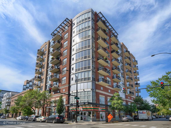 Front view of a multi-story residential building with balconies and retail stores on the ground floor.
