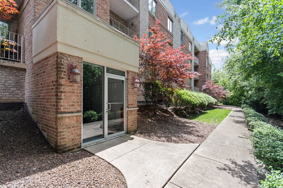 Front view of a multi-story brick building with glass doors and landscaped walkway.