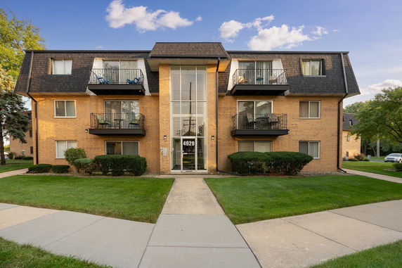 Front view of a multi-story apartment building with balconies and a central glass entrance.