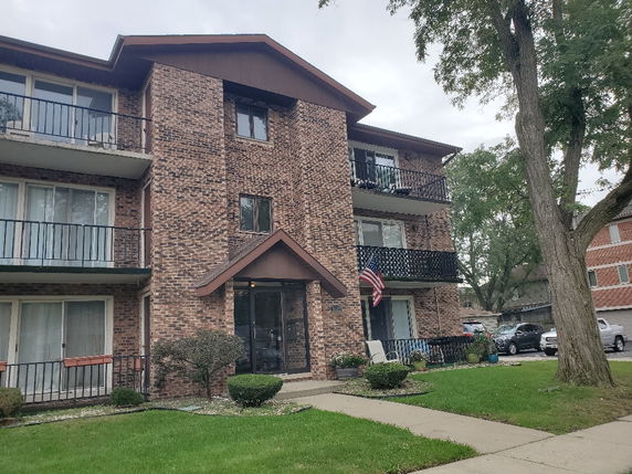 Front view of a multi-story brick apartment building with balconies.