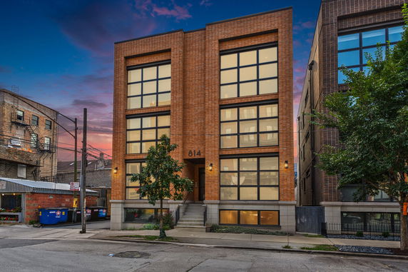 Front view of a modern multi-story brick building with large windows at dusk.