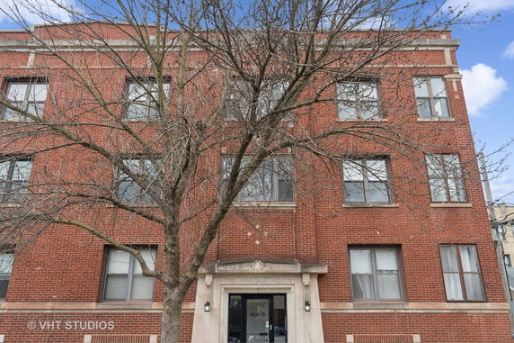 Front view of a brick apartment building with multiple windows and a central entryway.