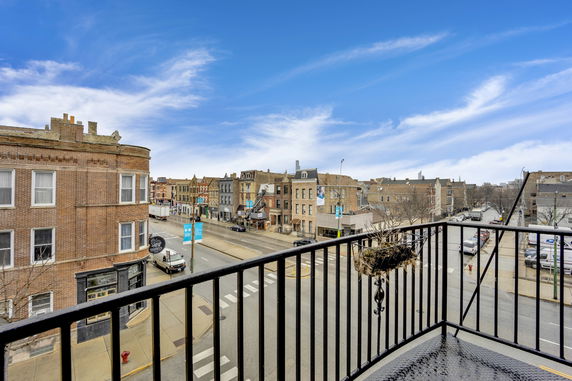 View from a balcony showing a street with buildings and vehicles in an urban area.