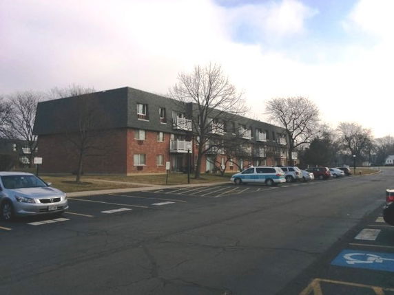 Front view of a three-story apartment building with parking spaces in front.