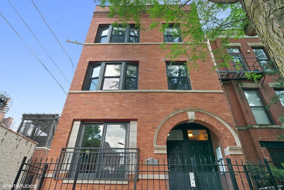 Front view of a multi-story brick building with black framed windows and an arched entrance.