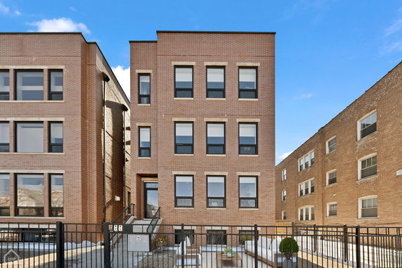 Front view of a three-story brick apartment building with a fenced entrance.