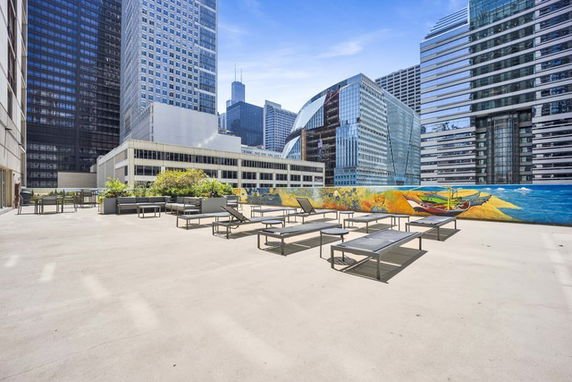 Rooftop terrace with loungers and a mural, surrounded by tall buildings.
