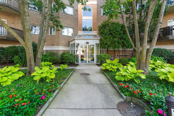 Front view of a multi-story building with glass entrance and surrounding greenery.