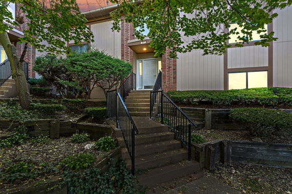 Front view of a house with brick and siding exterior, featuring a stairway leading to the entrance.
