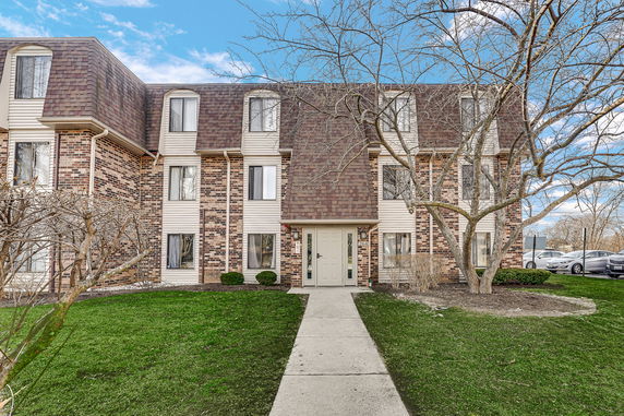 Front view of a multi-story brick building with a brown roof and several windows.