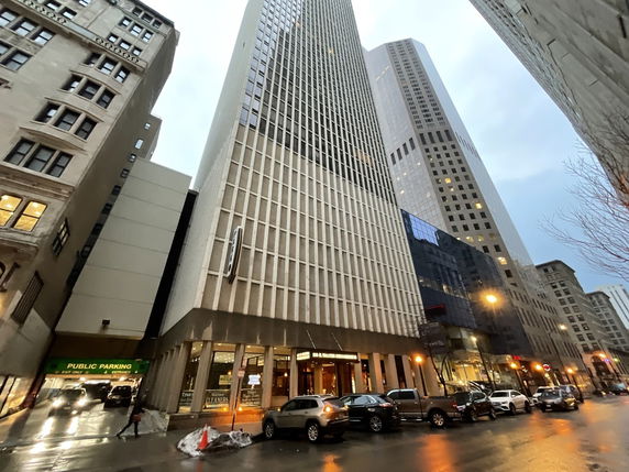 Front view of a tall building in a city with large windows and grid-like facade.