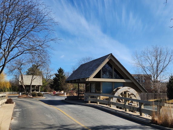 Front view of a structure with a wooden wheel and sloped roof by a road.