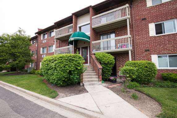 Front view of a multi-story brick apartment building with balconies and a green awning over the entrance.