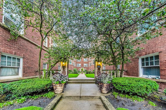 Front view of a multi-story brick building with landscaped walkway and illuminated entrance.
