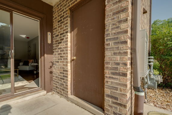 Brick exterior wall with a brown door and adjacent sliding glass door leading to an indoor living area.