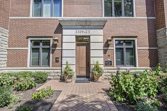 Front view of a brick house entrance with a wooden door and large windows.