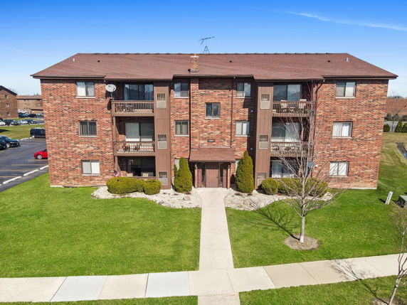 Front view of a three-story brick apartment building with balconies.