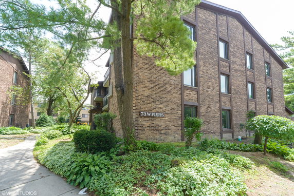 Front view of a multi-story brick building with rectangular windows and surrounding greenery.