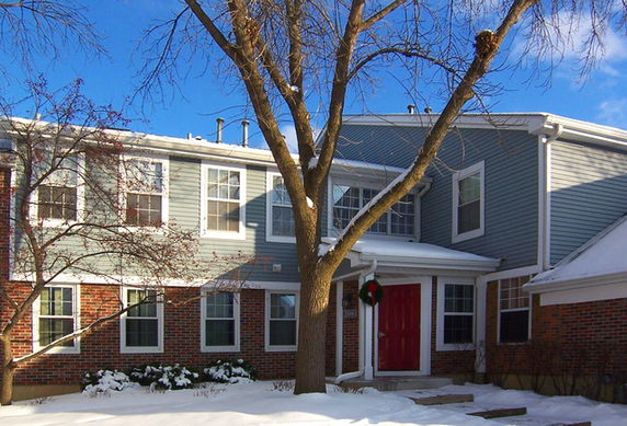 Front view of a two-story house with a red door and snow around.