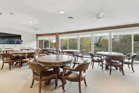 Room with round tables and chairs, large windows, and a wall-mounted TV.