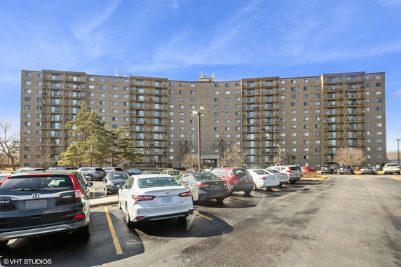 View of a multi-story apartment building with a parking lot in front.