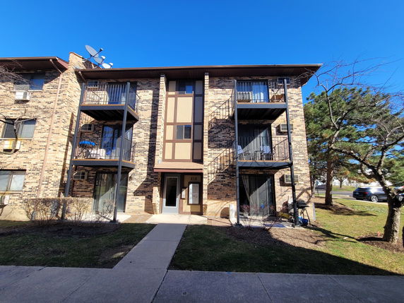 Front view of a multi-story apartment building with balconies and brick facade.