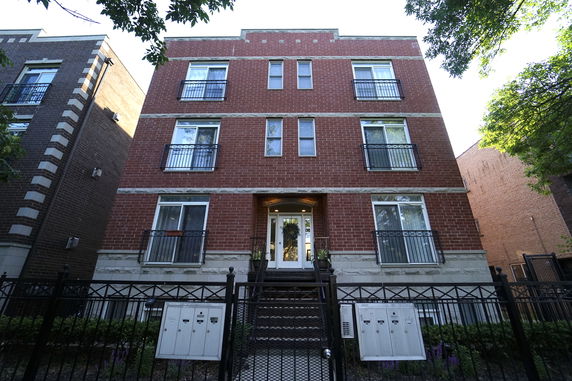 Front view of a three-story brick building with balconies and a gated entrance.