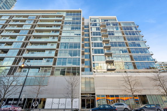 Front view of a modern high-rise building with glass balconies and commercial units on the ground floor.