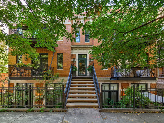Front view of a multi-story brick building with balconies and stairs leading to the entrance.