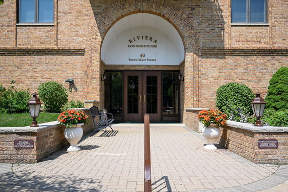 Front view of a brick condominium entrance with large wooden doors and decorative planters.