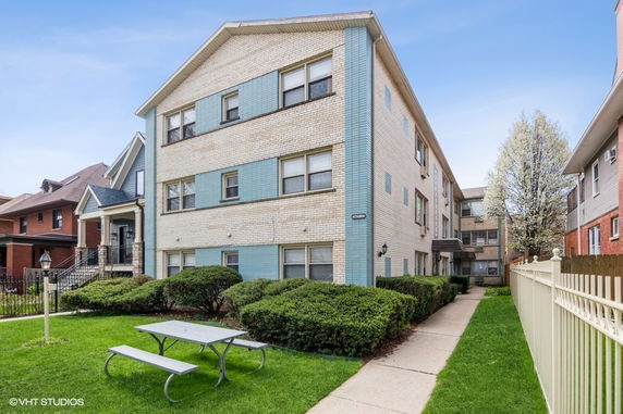 Front view of a multi-story apartment building with a light brick exterior and blue accents.