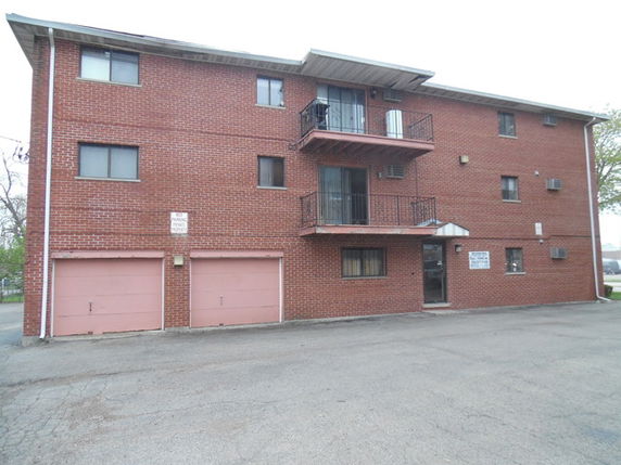 Front view of a three-story brick building with balconies and a double garage.