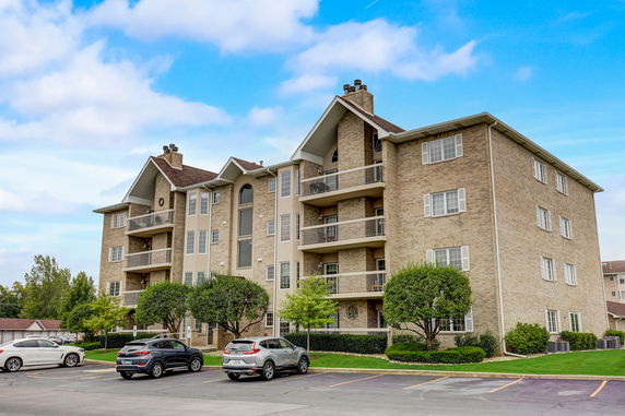 Front view of a multi-story apartment building with balconies and a parking area.