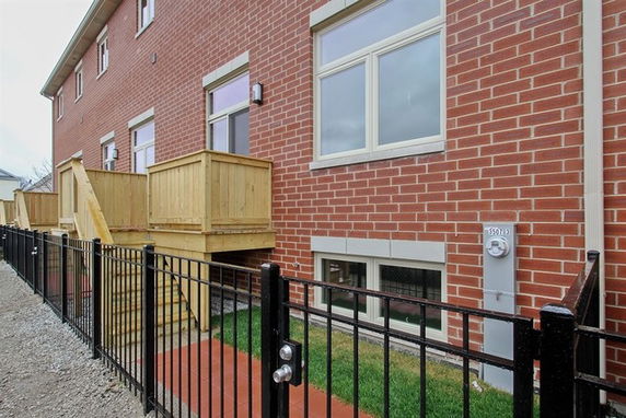 Front view of a multi-story brick house with wooden deck and fenced yard.
