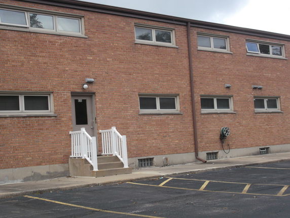 Front view of a two-story brick building with a small entrance and several small windows.