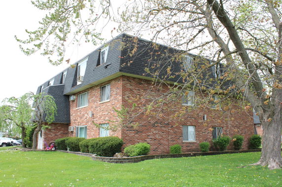 Front view of a brick apartment building with multiple floors and sloped roof.