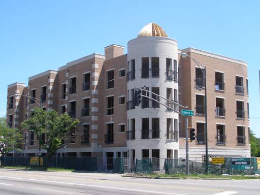 Front view of a multi-story building with a distinctive cylindrical corner section and a dome roof feature.
