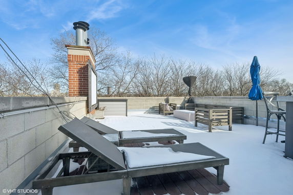 Rooftop patio with lounge chairs, a chimney, and patio furniture covered in snow.